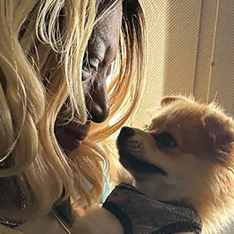 Woman holding a small, furry emotional support dog close to her face.