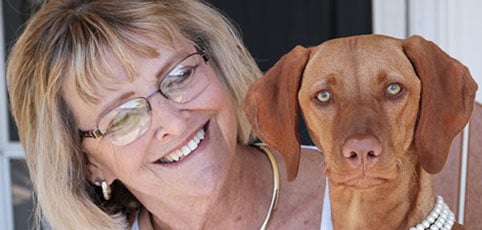 Woman in glasses smiling at a brown emotional support dog.