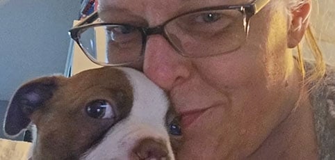 Woman in glasses kissing an emotional support dog on the forehead.